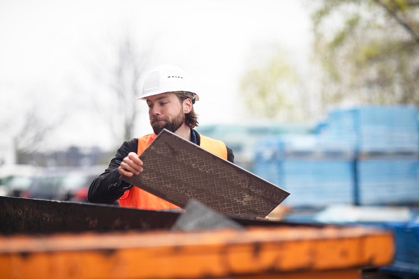 Mid adult male construction worker putting waste into waste skip